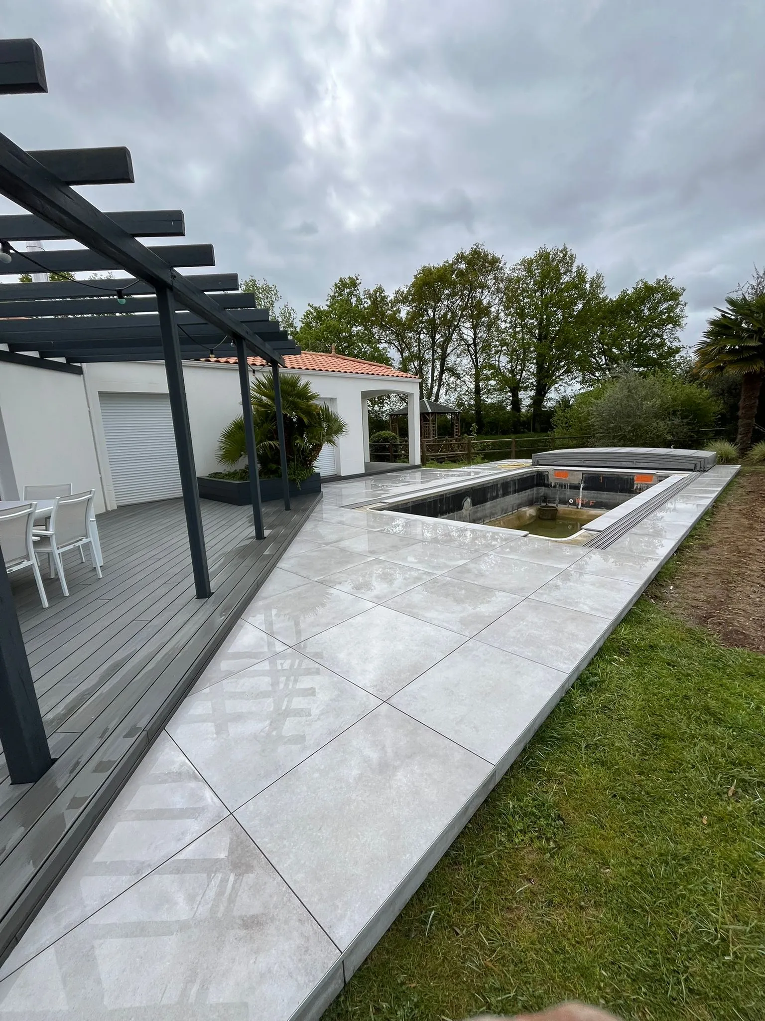 Terrasse carrelée et terrasse bois autour d’une piscine avec pergola