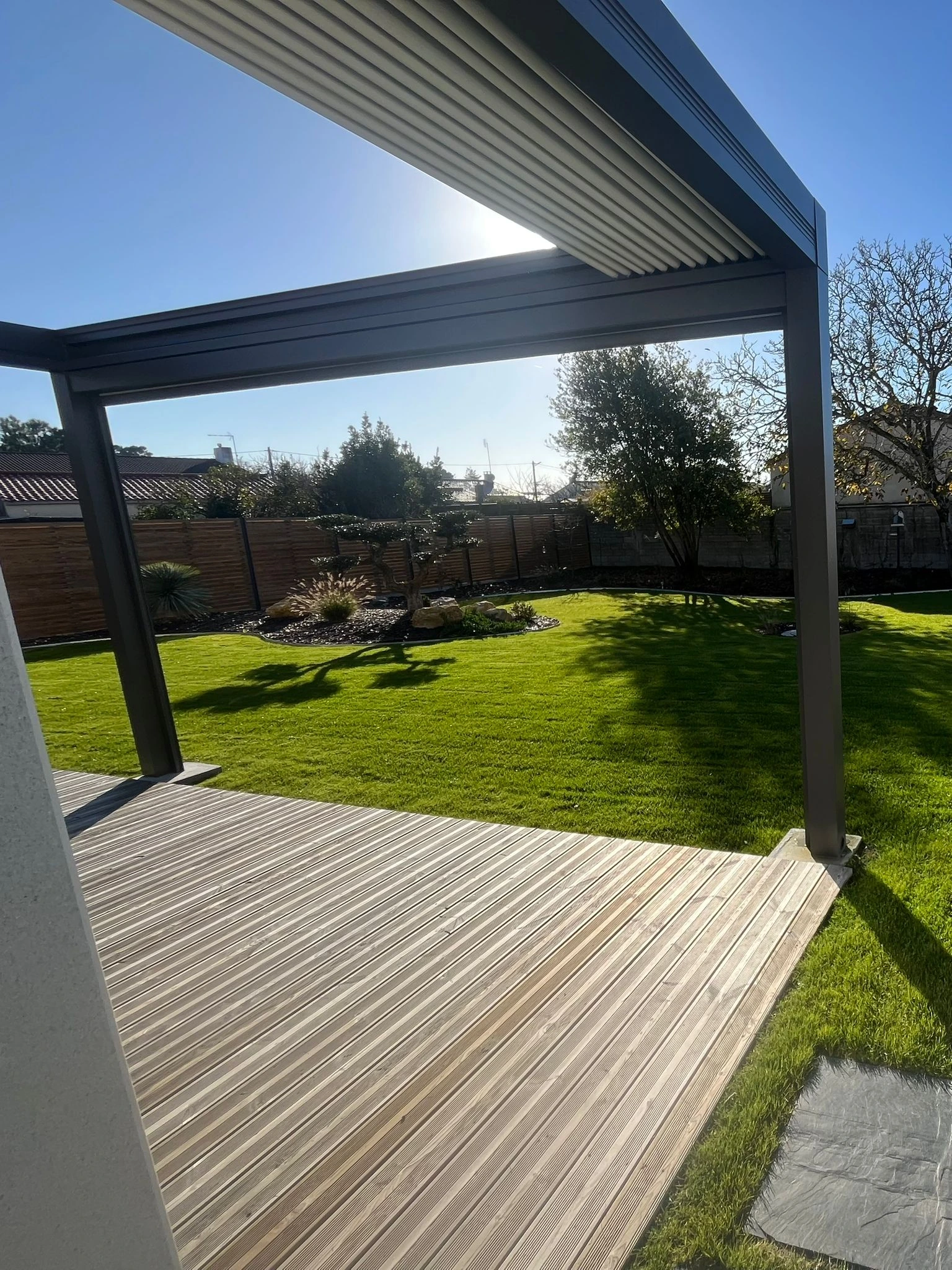 Pergola bioclimatique et terrasse en bois donnant sur un jardin paysager – aménagement extérieur à Pornic